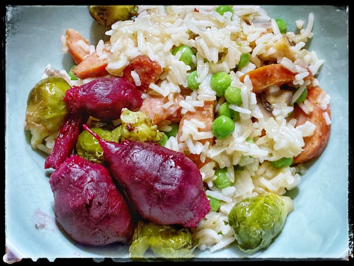 Maträtt med ris, räkor, gröna ärtor, rostade brysselkål och rödbetor på tallrik.