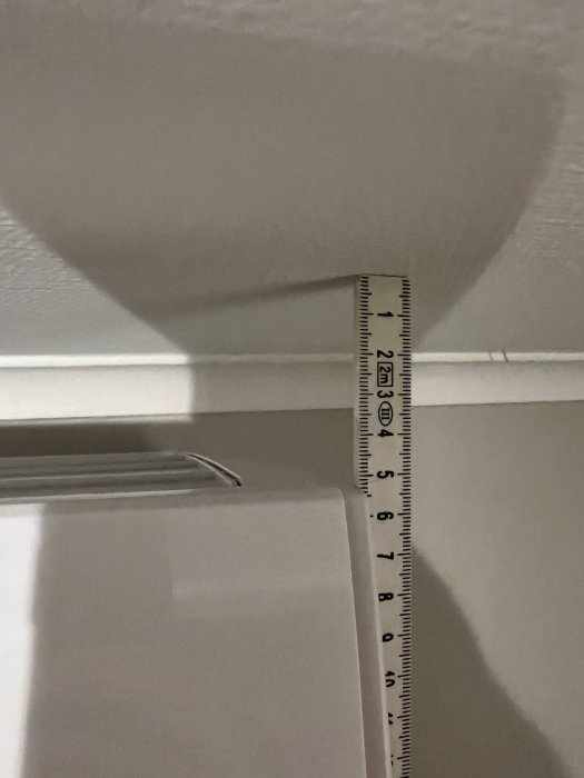 Mätsticka mot vit vägg och tak, visar cirka 22 cm, skugga bildar ett hjärta.