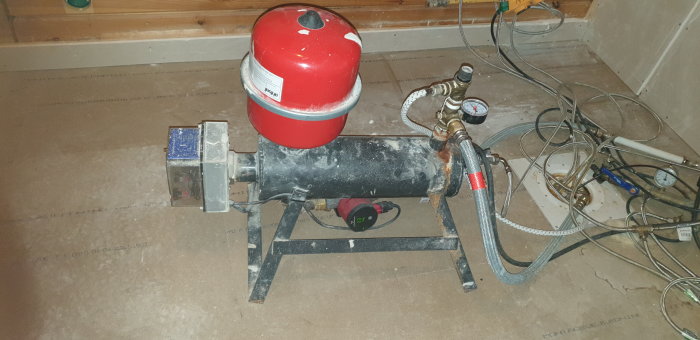 En vattenpump och expansionskärl för hemvattensystem på en verktygsbelamrad, dammig betonggolv i ett oavslutat utrymme.