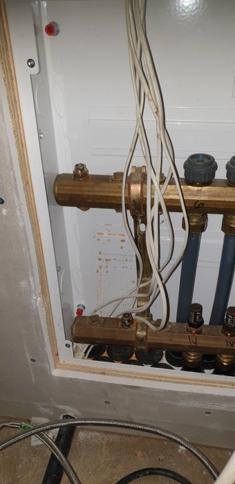 En öppen värmeskåp med synliga kopparledningar, kablar och mindre rostfläckar på bakväggen.