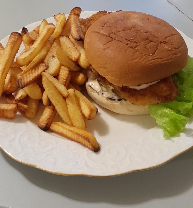 Tallrik med kycklingburgare och krinklad pommes frites. Snabbmat på vitt mönstrat porslin, enkelt mål.