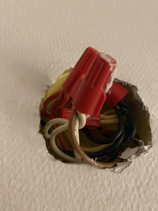 Elanslutningar i vägg, röda skarvhylsor, oskyddade, öppen hålighet, installationsarbete, potentiell säkerhetsrisk.