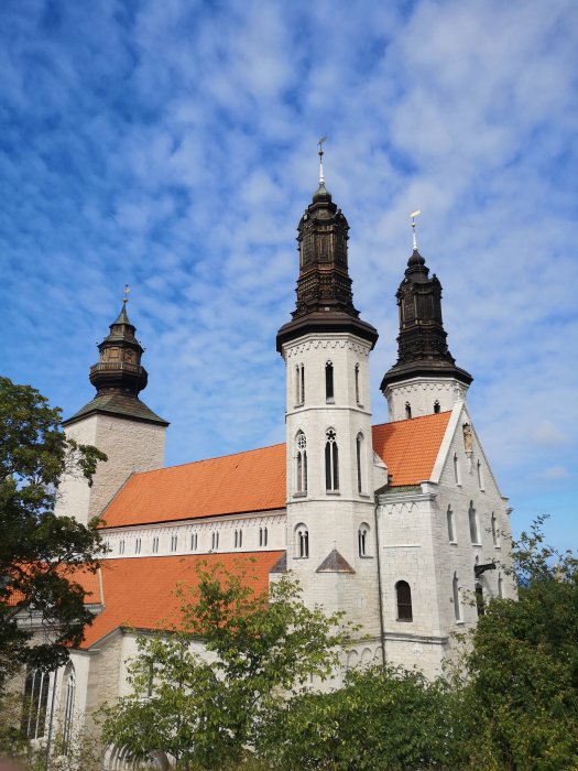 Ståtlig gammal kyrkobyggnad med två torn mot en blå himmel med vita moln.