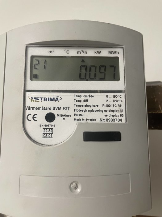 Värmemätare med digital display, visar temperatur och energiförbrukning, fast monterad på vägg.