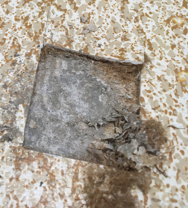 Ett gammalt, skadat golv med borttaget hörn som exponerar underliggande lager.