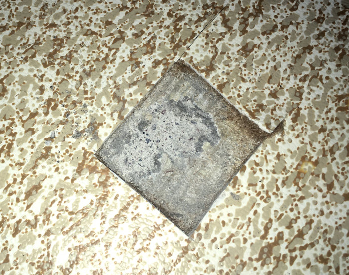 En gammal, nött platta på ett spräckligt mönstrat golv, slitage synligt, åldrade material, skrovlig yta, diskreta färger.