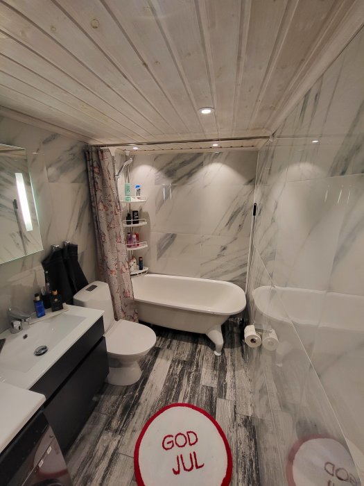 Ett modernt badrum med badkar, dusch, träpanel i taket, och textmatta "GOD JUL".