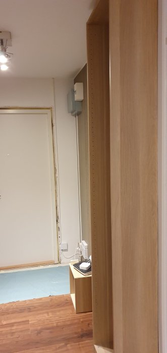 Inredningsprojekt med trähyllor, kabelgenomföring, skyddad golvdel och spacklad dörrkarm under renovering.