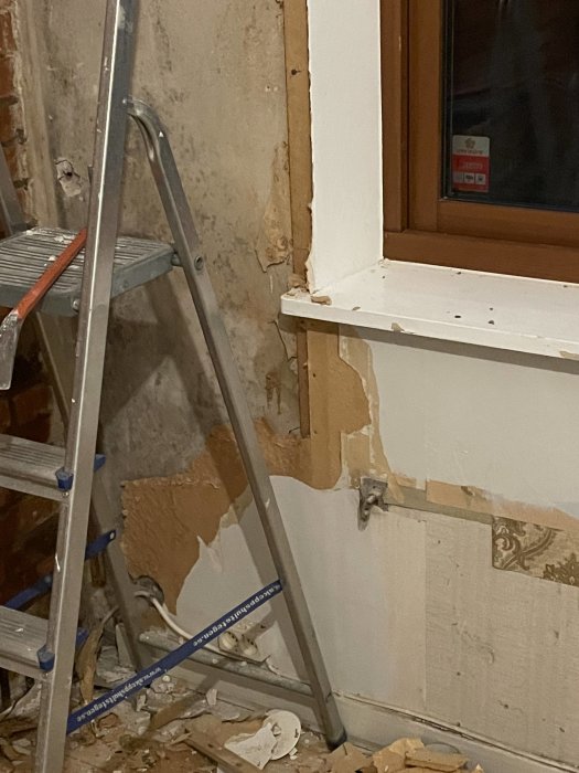 En stege, ett fönster och trasiga väggar; ser ut som en pågående renovering eller rivning inomhus.