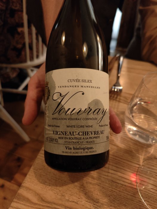 En flaska vitvin, "Vouvray", ekologisk, handhållen, bakgrund av restaurangmiljö, vinetikett med detaljer.