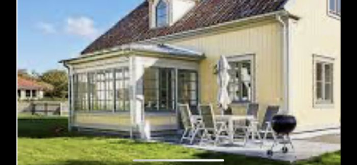 Gult hus med uterum, fönster, gräsmatta, vita stolar och en grill.