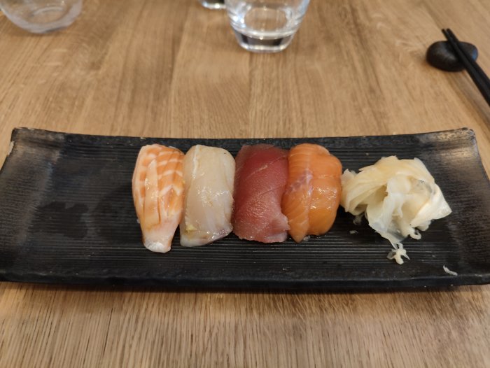 Fyra nigiri sushi på svart tallrik, med ingefära, på ett träbord.