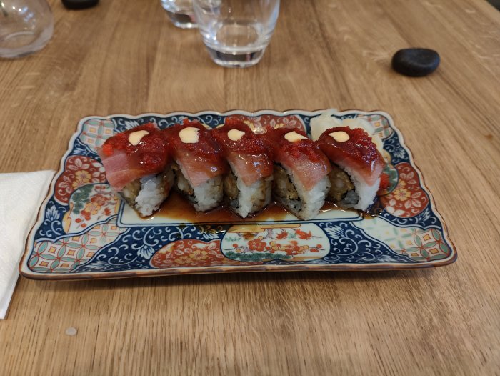 Färggrann sushi på mönstrad tallrik, rolig bild, träbord i bakgrunden.
