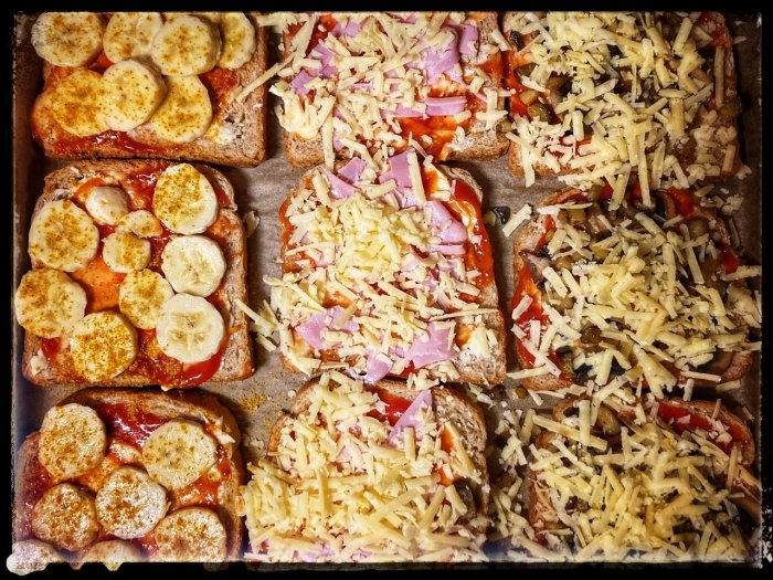 Fyra smörgåsar med olika pålägg och ost redo att grillas eller rostas.