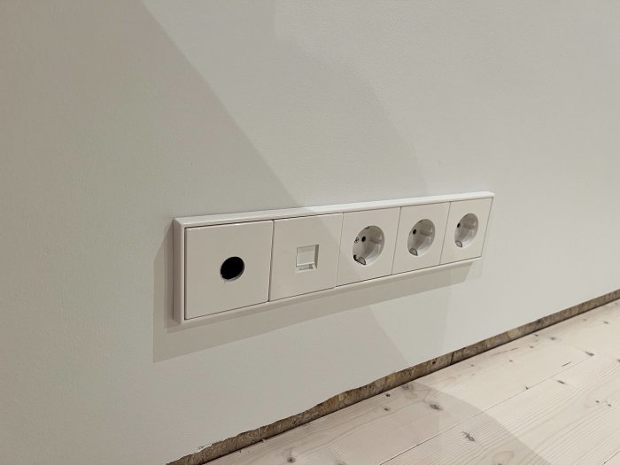 Vit fyrdubbel eluttag på en vägg ovanför ett trägolv.