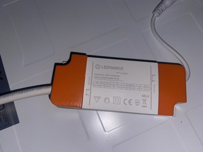 Elektronisk LED-konverter med kablar, orange och vit, tekniska specifikationer, ligger på vit yta.