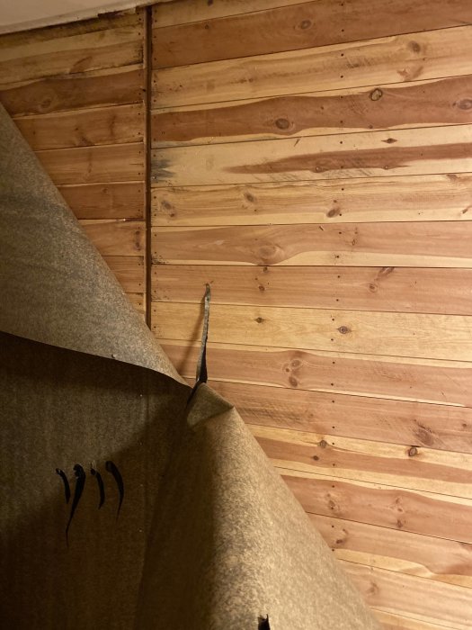 Trävägg och hörn med synligt isoleringsmaterial, inomhus, byggarbete pågår, något är avtäckt.