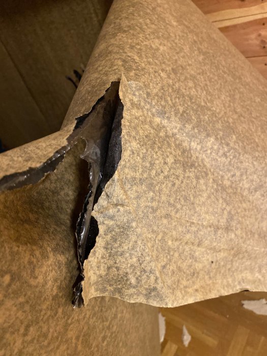 Brun kartong med slits eller rivet hål, skadad yta synlig, förpackningsmaterial, närbild, bristande kvalitet.