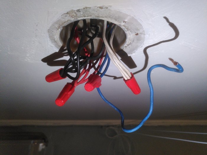 Öppen elektrisk anslutning i tak, oisolerade kablar med skarvhylsor, installationsarbete pågår, säkerhetsrisk.