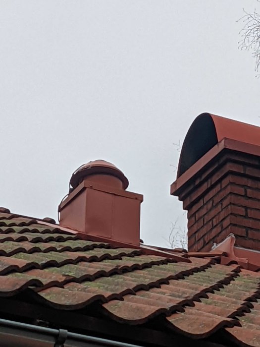 Tegelröd tak med skorstenar och takkupa. Mulen himmel. Klassisk byggnadsstil.