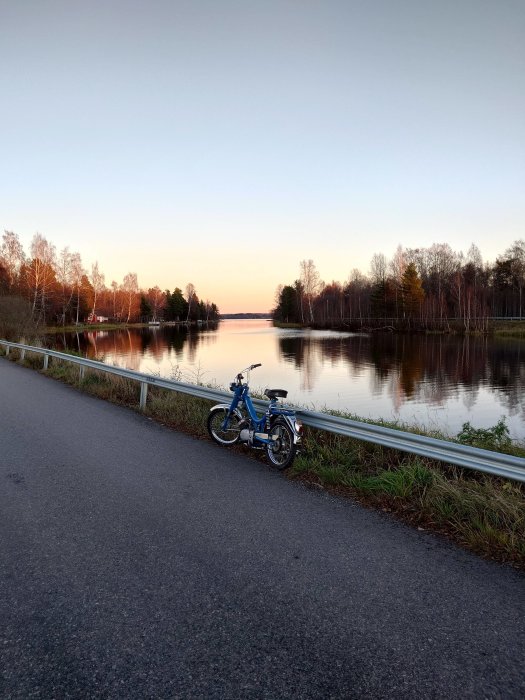 Moped bredvid landsväg, sjöreflektion, skog, solnedgång, klart väder, höst.