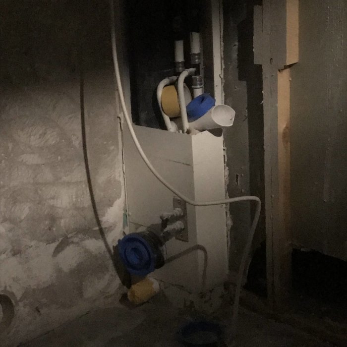 Mörkt utrymme med rör och installation, delvis demonterat, i en byggnad eller källare.