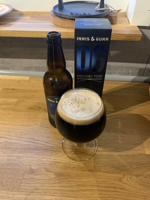 Ölflaska och glas med mörkt öl, paket med texten "Innis & Gunn," träyta, bakgrund med köksredskap.