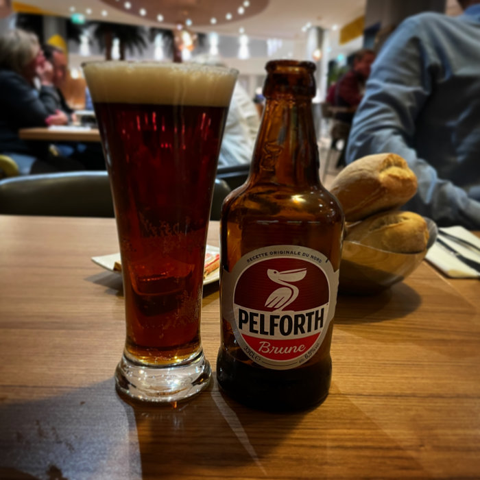 En flaska Pelforth Brune öl och ett fyllt glas på ett bord, med suddig restaurangbakgrund.