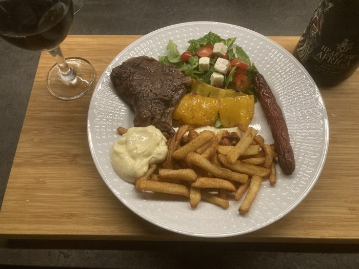 Middagstallrik med biff, pommes, sallad, grillad paprika, korv, bearnaisesås. Rödvin och en ölflaska.