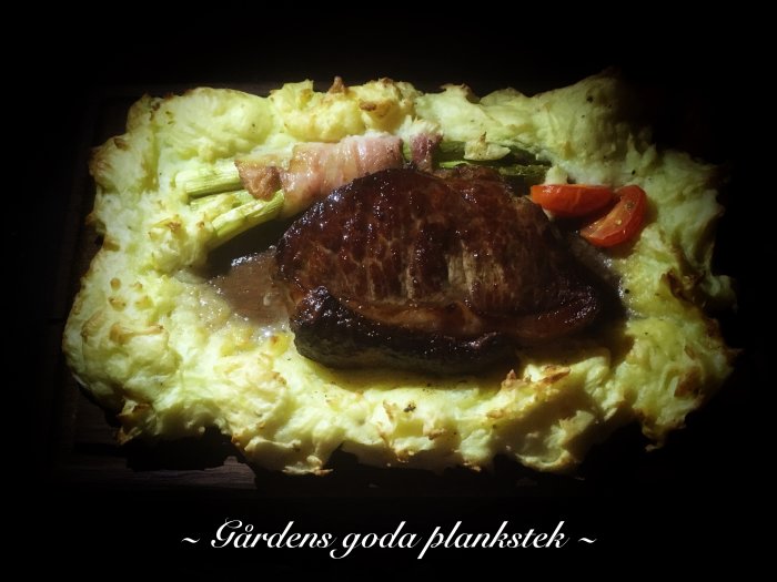 Ett traditionellt planked steak (plankstek) med biff, mosade potatis, bacon och tomat på träplanka.
