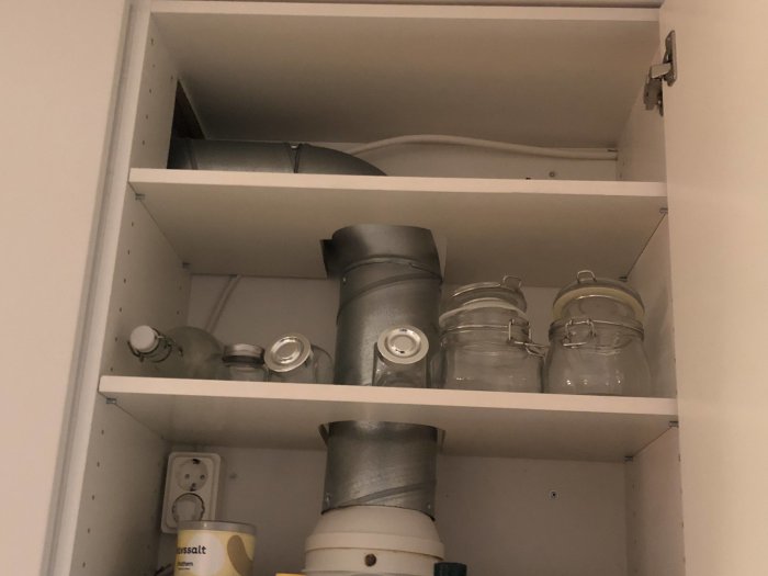Vit köksskåp med förvaringsburkar, ventilationsrör och en behållare med grovsalt.