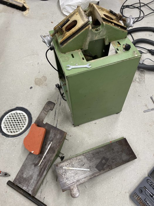 Nedmonterad grönmålad maskin, verktyg, komponenter utspridda på en smutsig verkstadsgolv.