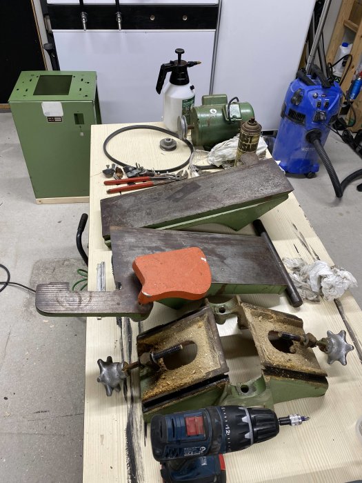 Verkstadsbord med verktyg, skruvstycke, borr och andra maskiner. Arbetsplats kan indikera metallarbete eller hantverksprojekt.