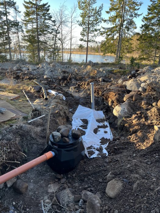 Grävd jord, stenar, plaströr, svart behållare; konstruktion eller reparation av en installation utomhus nära vatten.