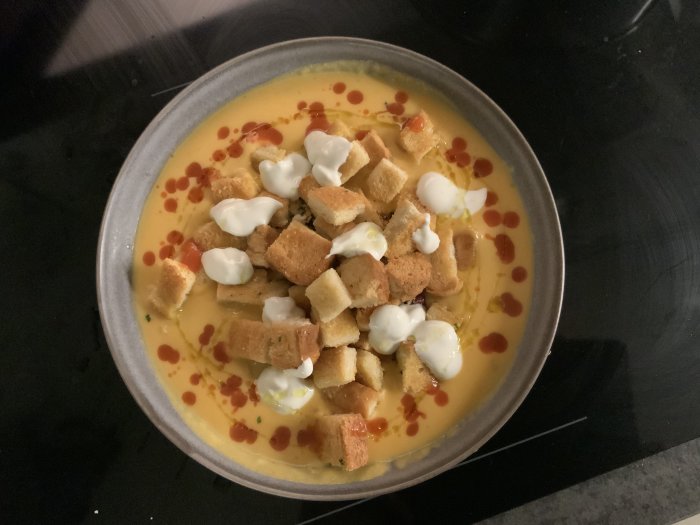 Soppa med krutonger, gräddklickar och röd sås i en skål.