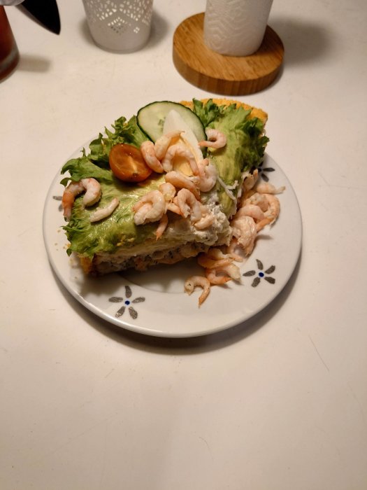 En smörgås med sallad, räkor, gurka och tomat på ett dekorerat fat.
