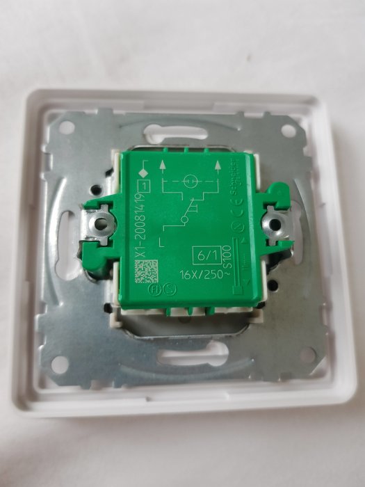 Grön elektrisk komponent i vit plastbehållare. Märkt med schematisk diagram, produktinformation och säkerhetscertifieringar.