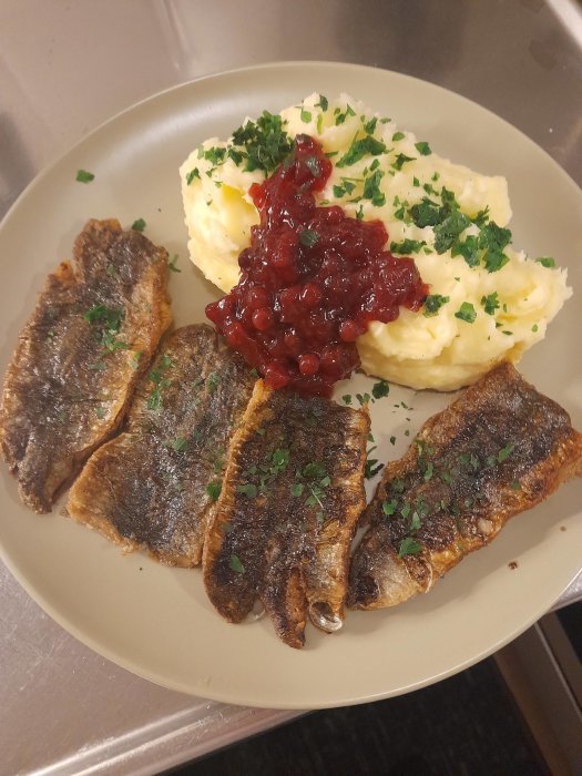 Stekt fisk, potatismos, lingonsylt och hackad persilja på tallrik. Klassisk nordisk måltid.