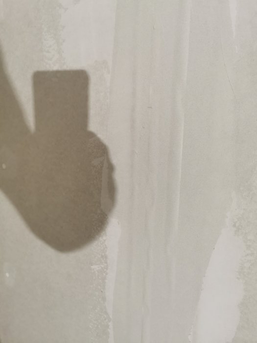 Kuva seinästä, jossa nauha kuplii toisen tasoituskerroksen jälkeen. Seinän pinnassa varjo.