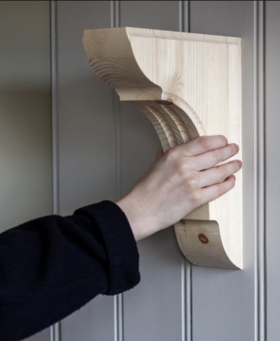En hand griper ett ovanligt format trähandtag fastsatt vid en ljusgrå dörr.