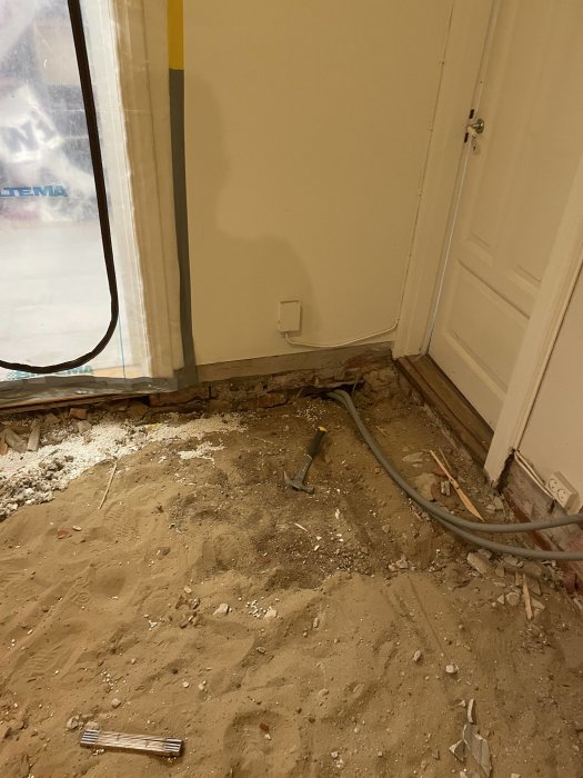 Renoveringsarbete, rördragning, sandspridning, verktyg, oavslutat golv, exponerad vägg, dörr, konstruktionsröra.