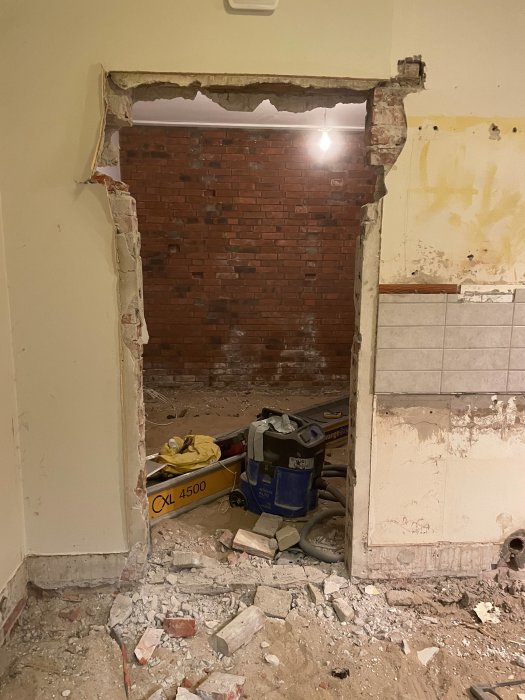 Renovering inne, rivet väggparti med synlig tegelvägg, rör och byggavfall på golvet.
