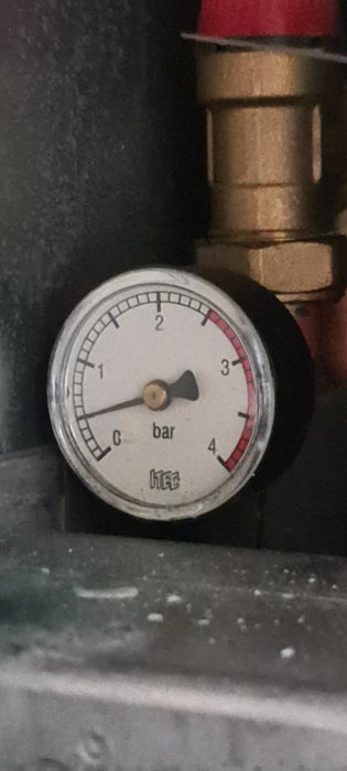 Tryckmätare. Visar cirka 1.5 bar. Mässingskoppling. Röd säkerhetslock. Möjlig industriell eller VVS-inställning.