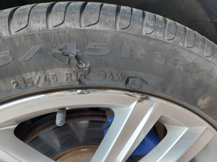 Bildäck med skada och inbäddat föremål nära texten "235/45 R18 94W".