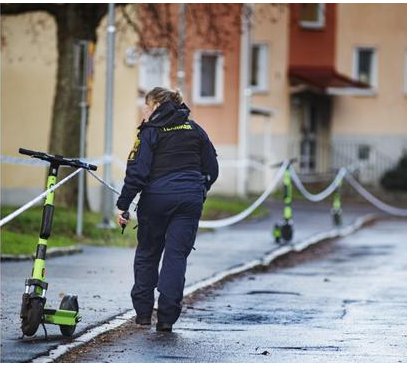 Polis på gata, avspärrning med band, verkar undersöka en händelse, elektrisk sparkcykel framför, bostadsområde i bakgrunden.