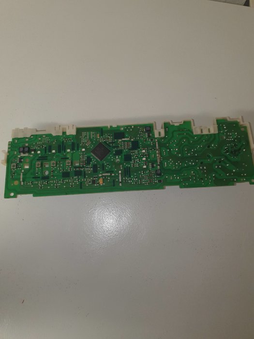 Kretskort med integrerade kretsar och elektroniska komponenter på vitt underlag.