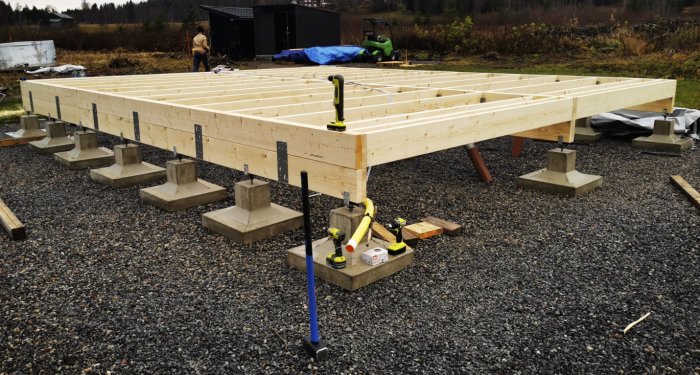 Grundkonstruktion av trä på betongplintar, verktyg runtom, arbetsplats utomhus, byggnation i tidigt skede.