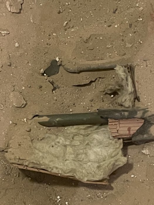 Gamla föremål i smuts, möjligtvis arkeologisk utgrävning, med fragment och verktyg synliga.
