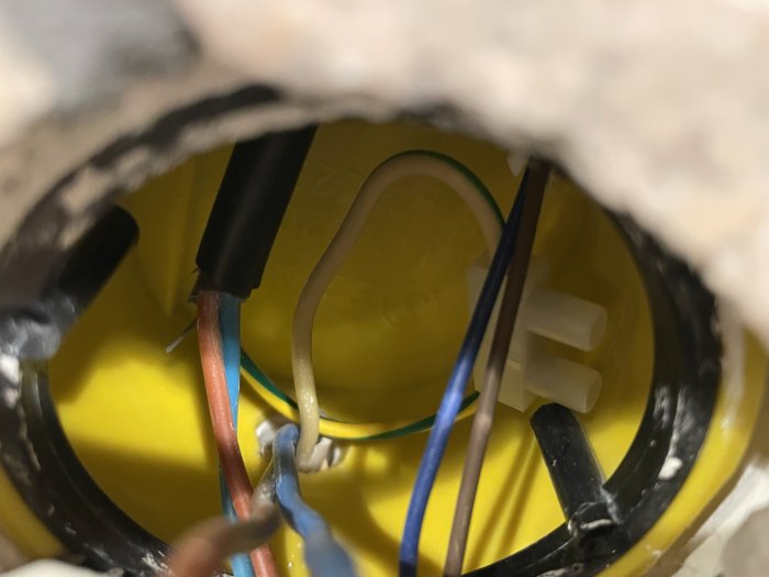 Närbild av elektriska ledningar och kontakter inuti en vägg med synlig gul väggdosa.