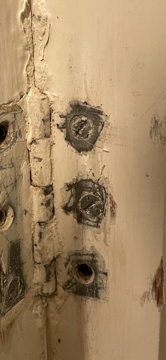 Sliten dörrkarm med gamla gångjärnsskruvar, spackel, slitna kanter och skrapmärken. Nötta, föråldrade byggnadsdetaljer.